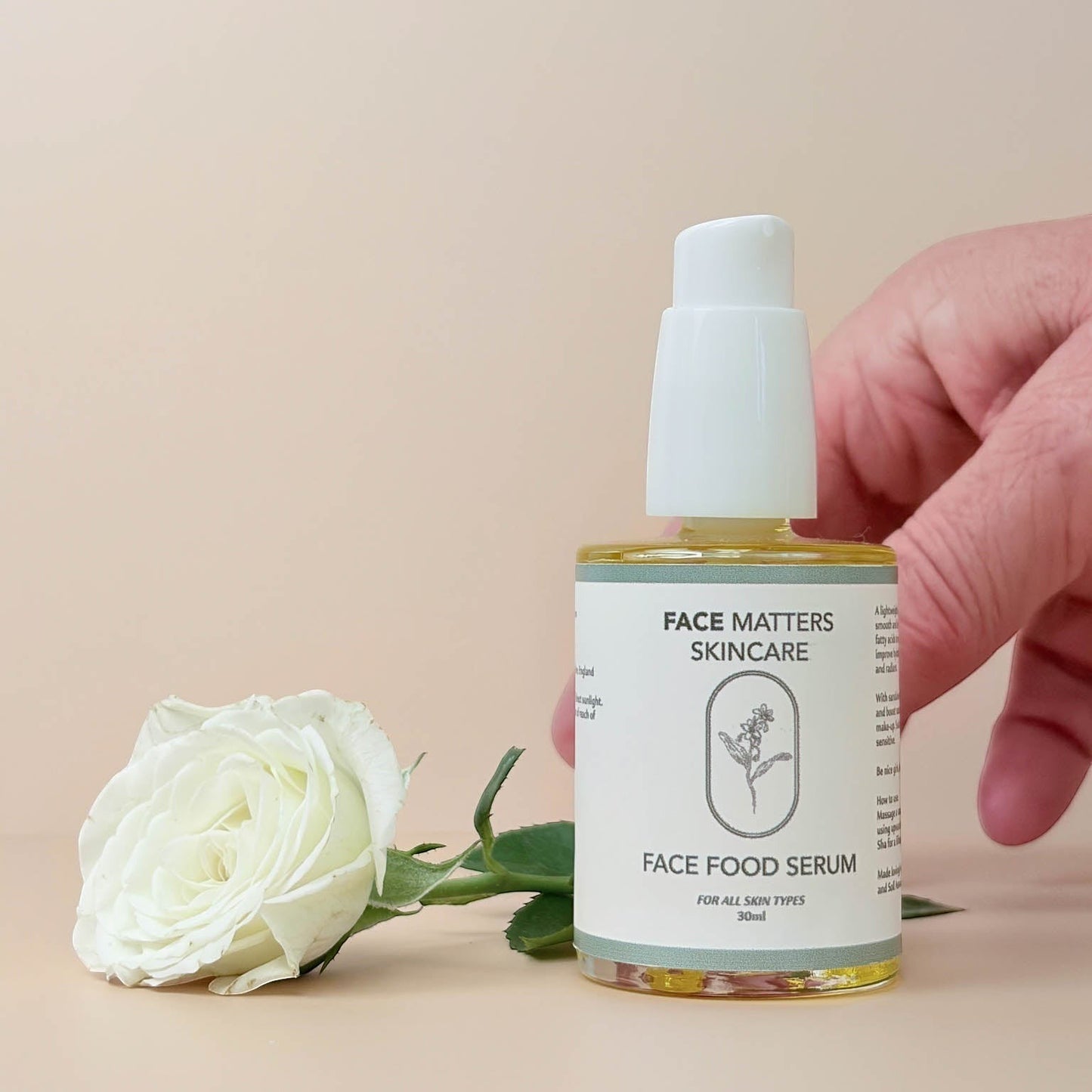 Face Matters Skincare Face Food Serum in a glass bottle with a white pump, next to a white rose on a beige background.