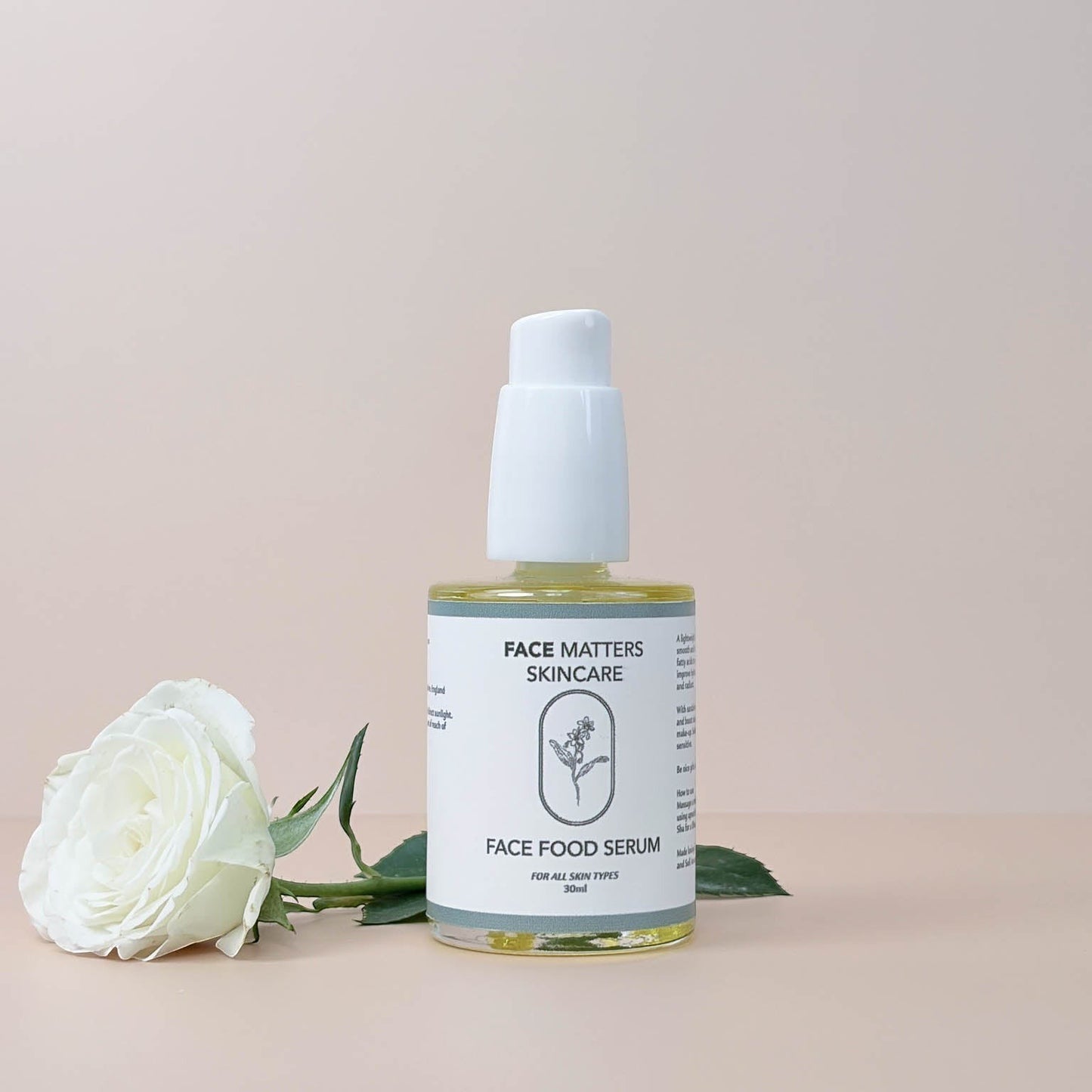 Face Matters Skincare Face Food Serum in a glass bottle with a white pump, next to a white rose on a neutral background.