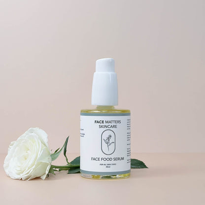 Face Matters Skincare Face Food Serum in a glass bottle with a white pump, next to a white rose on a neutral background.